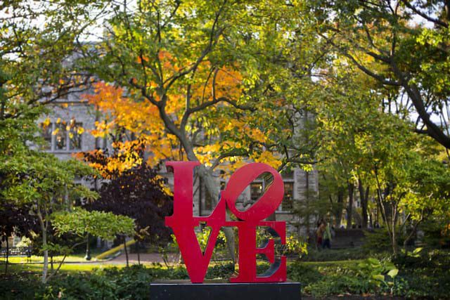 Red "LOVE" sculpture by Robert Indiana in a park setting with autumn trees in the background.