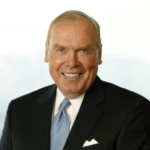 Headshot of a person wearing a dark pinstripe suit, light blue tie, and white shirt, smiling against a light background.