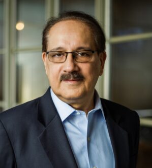 Headshot of a person wearing glasses, a navy blue blazer, and a light blue shirt, with a neutral expression.